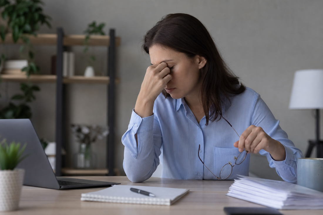 Exhausted adult sitting at a desk with head lowered and hand on forehead